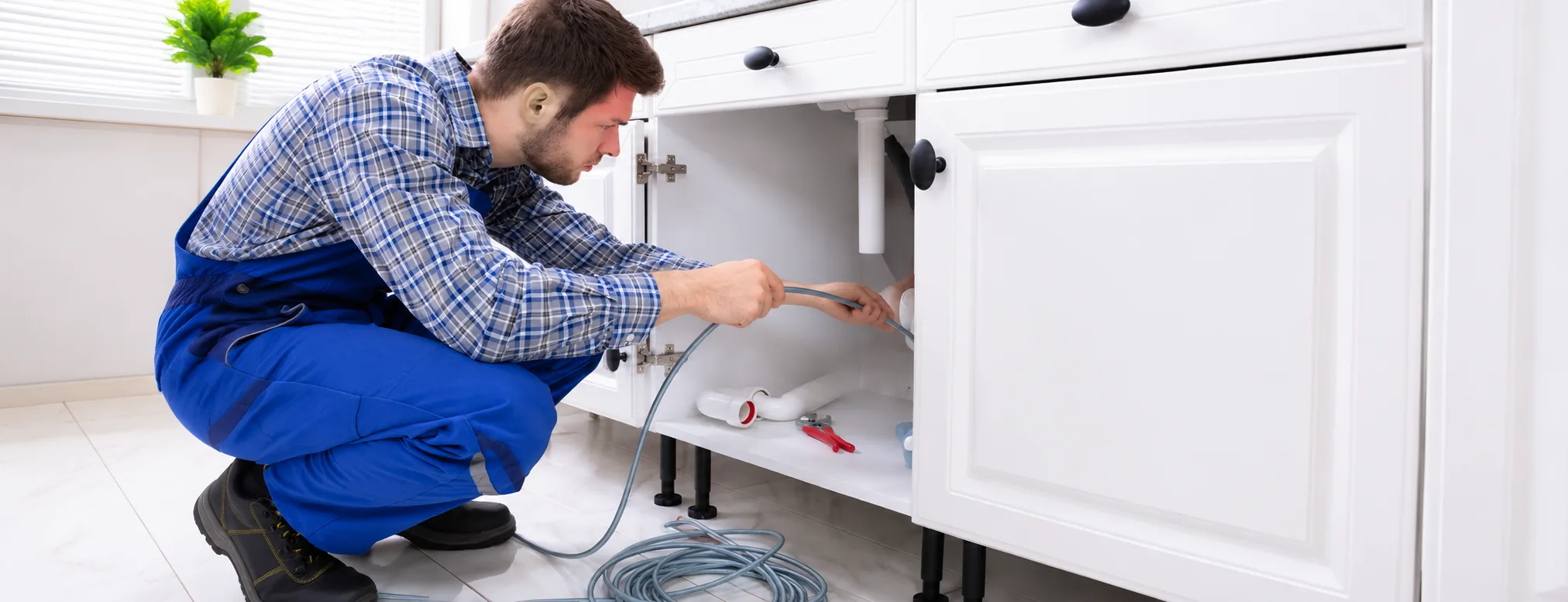 Plumber clearing a kitchen sink waste pipe under the cabinet