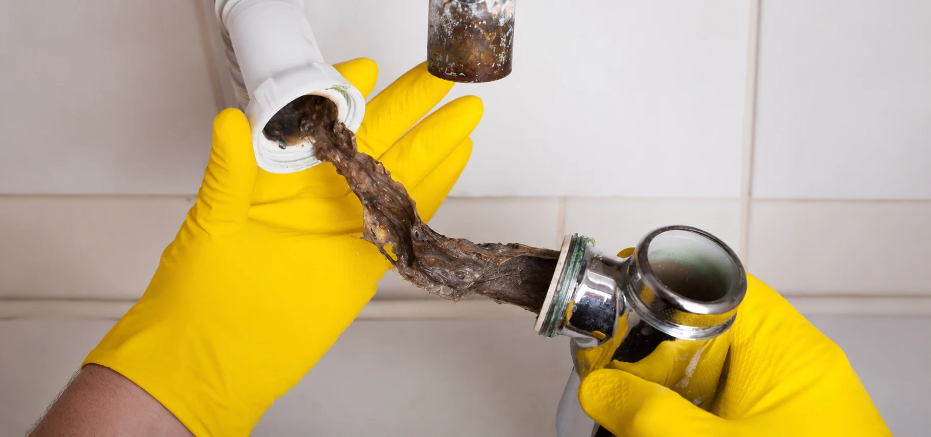 Gloved hands pulling a hair and grease clog from a basin waste trap