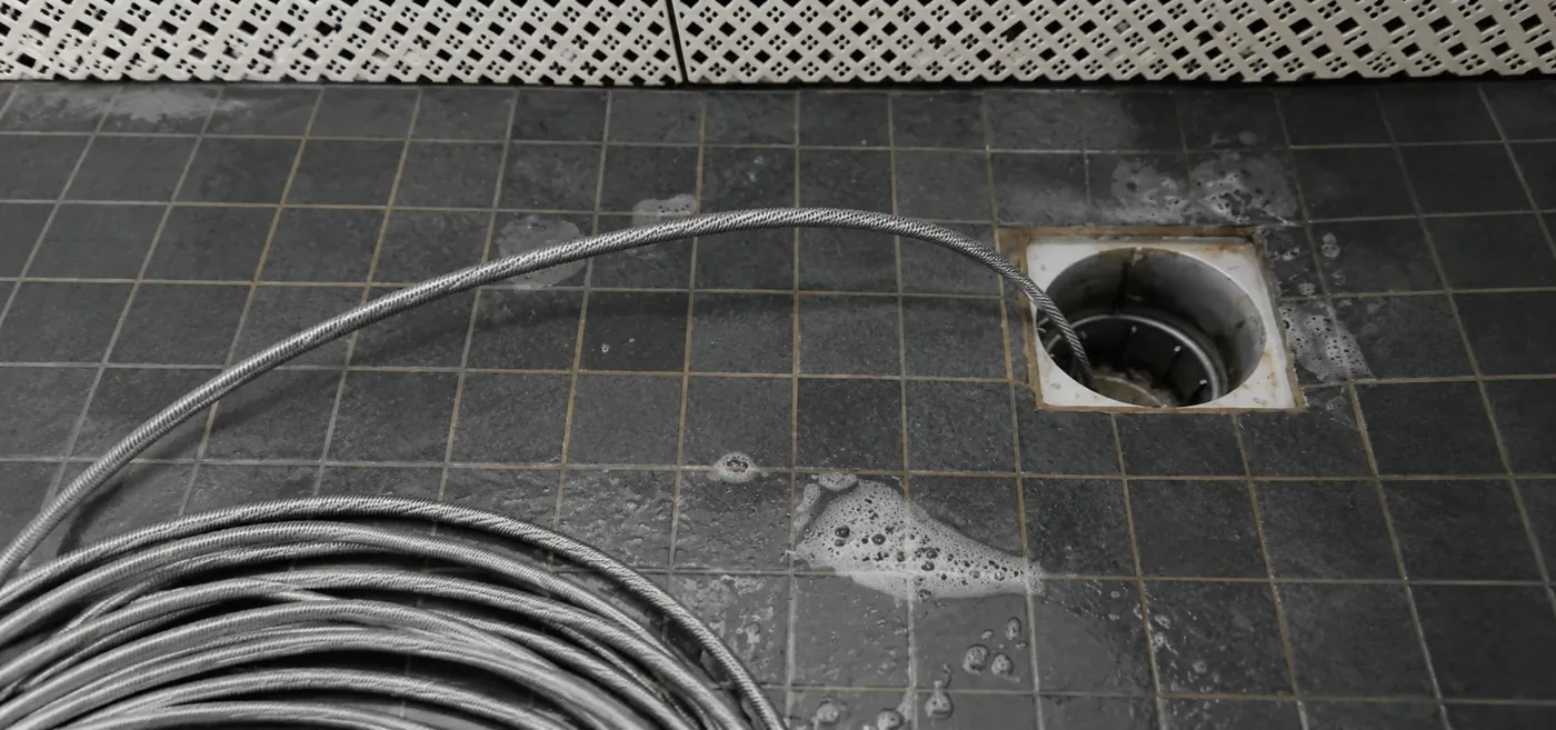 A coiled steel drain cable beside a floor drain